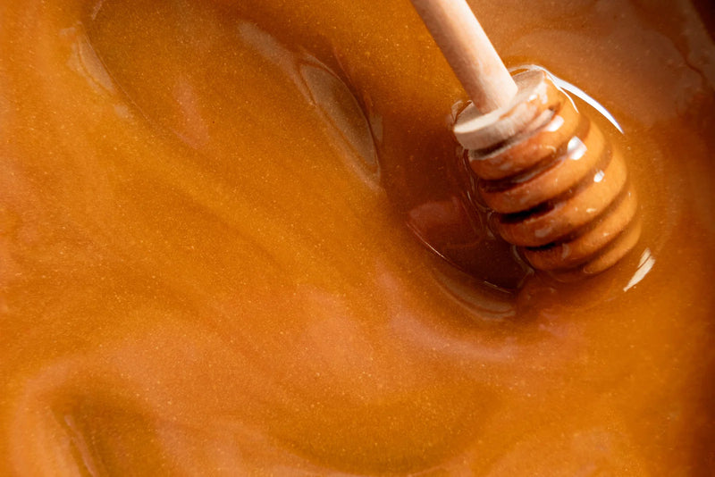 Close-up of a wooden honey dipper resting in glossy amber honey.
