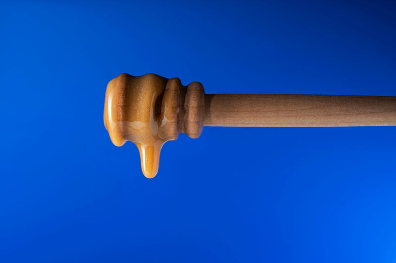Honig tropft von einem Holz-Honiglöffel vor blauem Hintergrund.