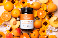 Manuka Honig UMF™ 10+ MGO 263+ Glas umgeben von Orangen, Pfirsichen und Blumen – Flat-Lay