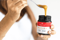 Hand hält geöffnetes Manuka Honig UMF™ 15+ MGO 514+ Glas – Löffel mit tropfendem Honig in Nahaufnahme