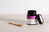 Geöffnetes Glas Manuka Honig UMF™ 24+ MGO 1122+ mit Holzlöffel auf neutralem Hintergrund