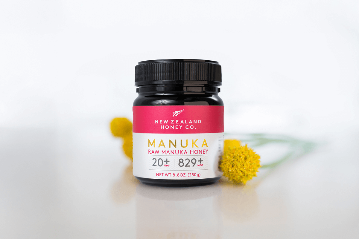 Manuka Honig UMF™ 20+ MGO 829+ Glas auf lila-rosa Untergrund mit Geschenkbox im Hintergrund