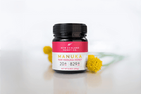 Manuka Honig UMF™ 20+ MGO 829+ Glas auf lila-rosa Untergrund mit Geschenkbox im Hintergrund