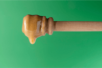 Nahaufnahme: Manuka Honig UMF™ 28+ MGO 1450+ tropft vom Holz-Honiglöffel vor grünem Hintergrund