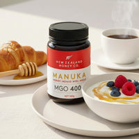 Manuka Honig MGO 400+ Glas neben Joghurt mit Beeren, Croissant und Kaffee – Frühstücksszene